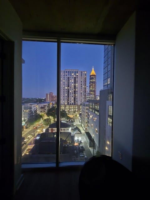 View from an interior room through large windows overlooking an illuminated city skyline at dusk with a prominent golden-topped skyscraper