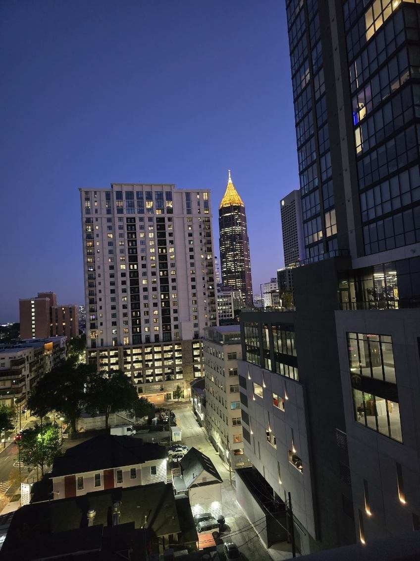 Evening cityscape showing illuminated skyscrapers with a distinctive gold-topped building in the center, surrounded by modern office and residential towers at dusk