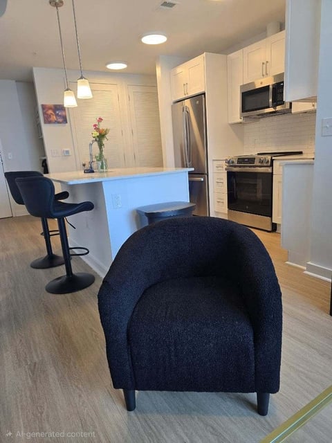 Modern kitchen and living area with blue accent island, stainless steel appliances, white cabinetry, and a dark navy accent chair in foreground